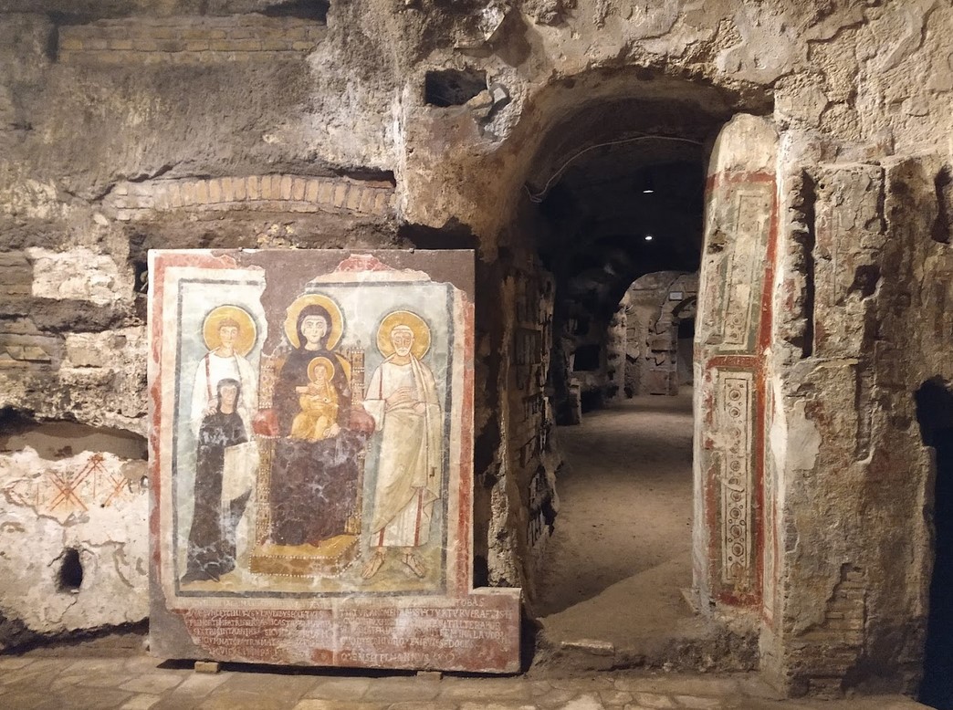 Wall painting from the Catacombs of Commodilla in the so-called Tomb of Turtura, mid-6th century. The fresco depicts the Madonna and Child seated on a golden stool, with the figures of Saints Felix and Adautto and the donor, Turtura. An inscription runs along the lower border: 'Your name is Turtura, and truly you were a real turtle-dove.'